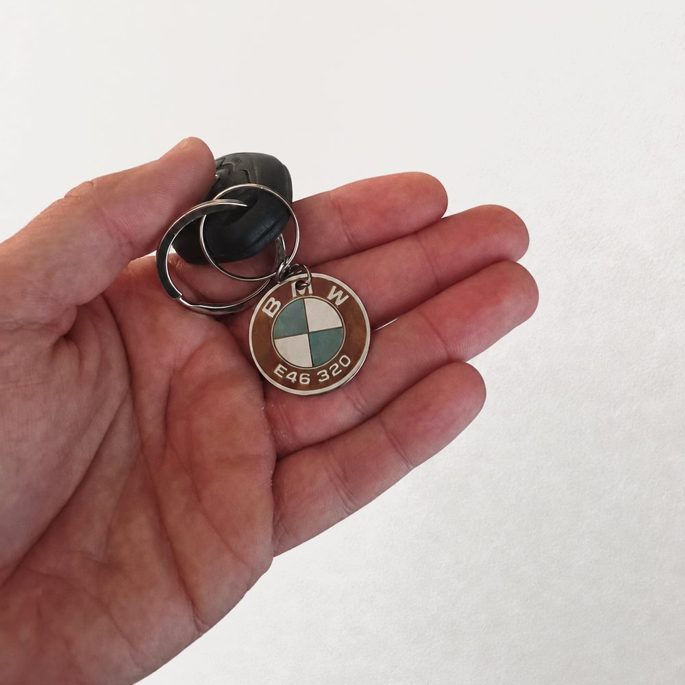 Hand holding a round steel keyring engraved in colour with a BMW badge and model code